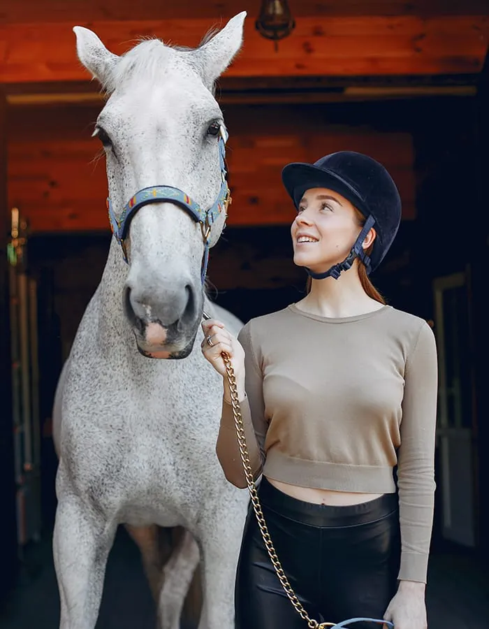 Rider standing beside a grey horse in the stable